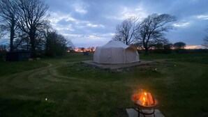 A tent in a grassy field with a fire pit nearby.