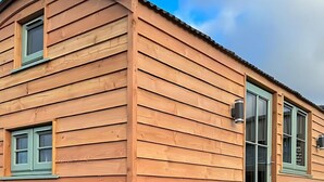 Une maison mobile en bois, dotée d’un toit incurvé, d’une porte d’entrée avec un panneau de verre et d’un petit escalier menant à l’entrée.