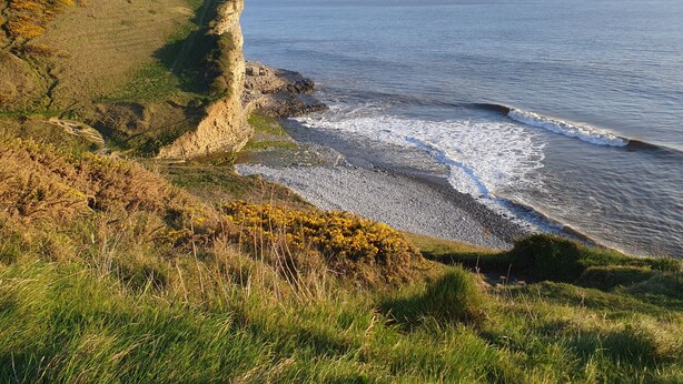 Un paysage côtier caractérisé par une falaise imposante et une plage de galets.