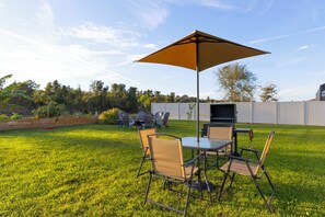 Eine Terrass mit Tisch und Stühlen, einem großen Sonnenschirm und einem Grill.