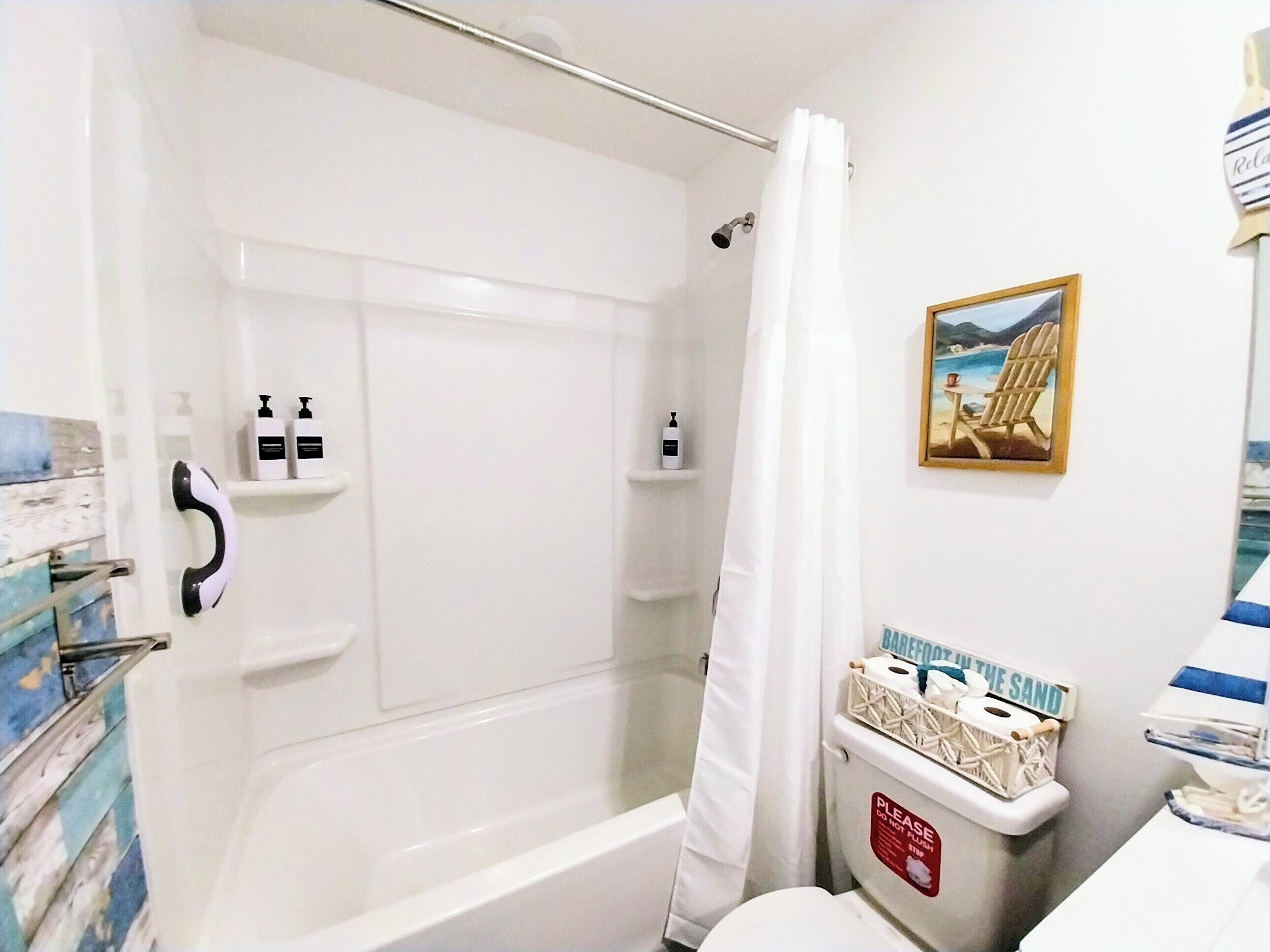 A bathroom with a bathtub, shower curtain, and a toilet with a sand-themed decoration.