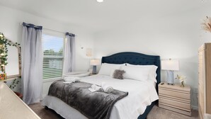 Un dormitorio ordenado con cama, mesitas de noche, cómoda y ventana con cortinas.