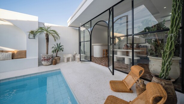 Et moderne poolområde med en glasindhegnet patio, fletstole og krukker med planter.