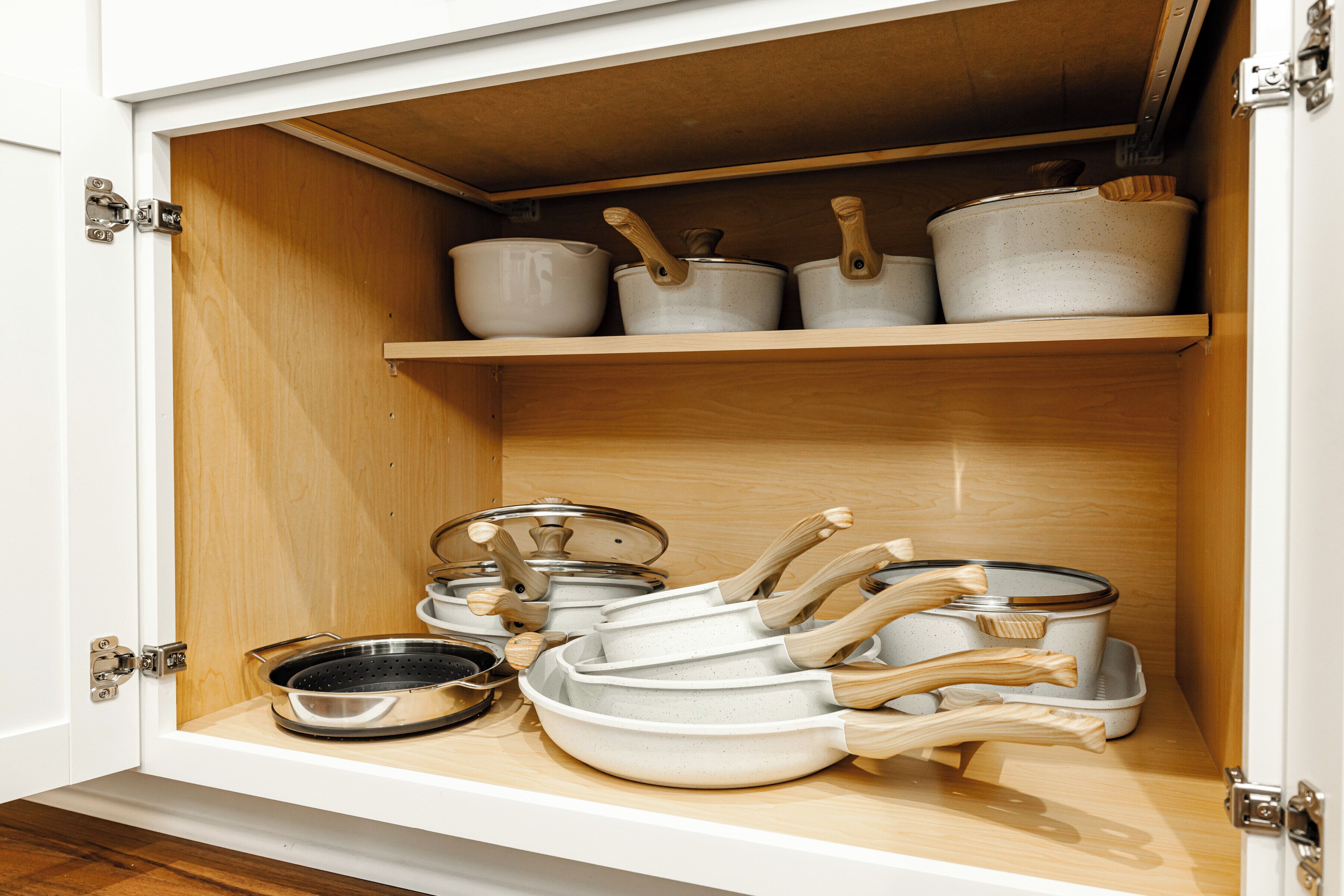 A kitchen cabinet with various cookware items including pots, pans, and a colander.