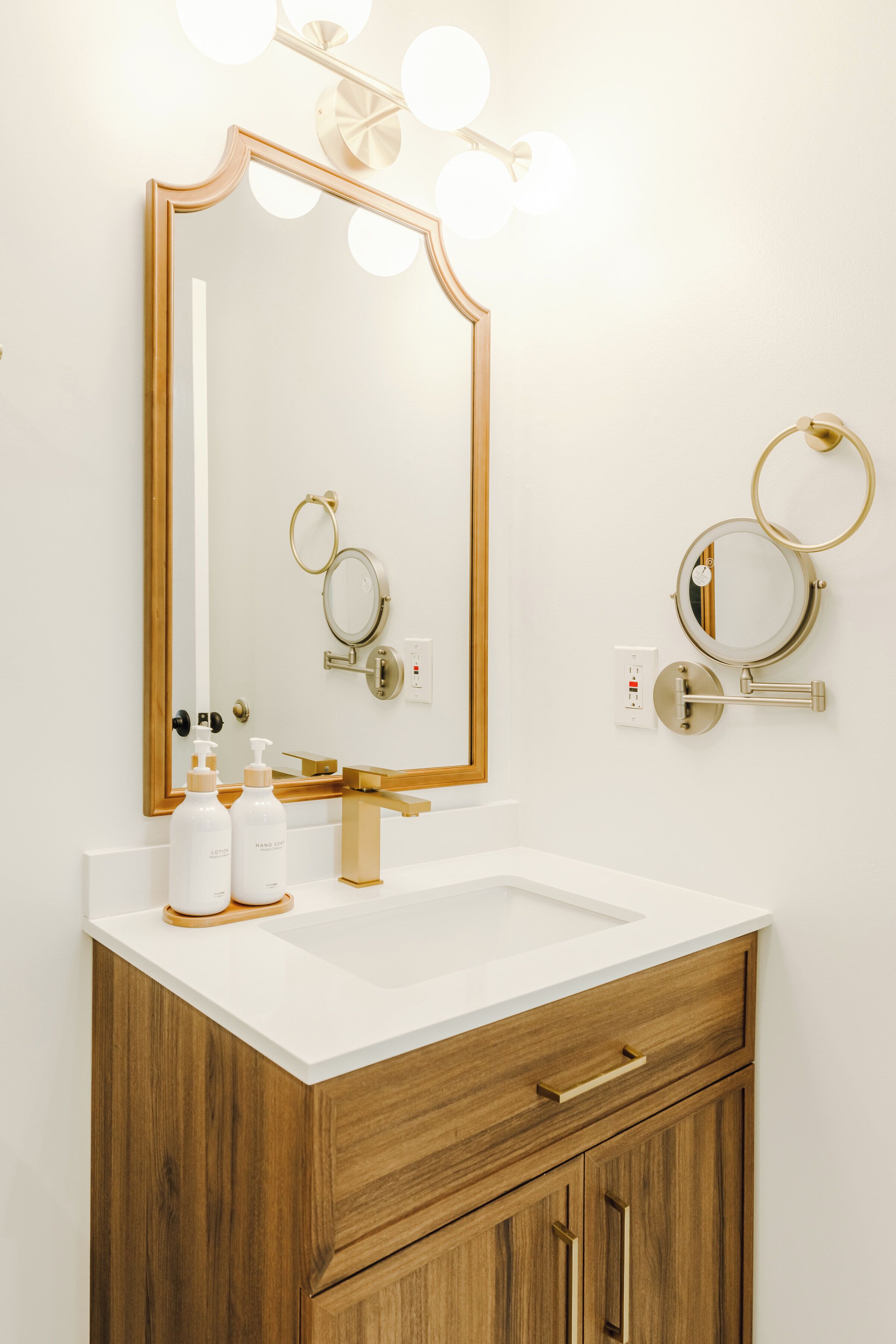 Ein Badezimmer mit einem großen Spiegel, zwei Wandleuchten, einem Waschbecken und Holzschränken.