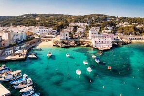 A coastal town with white buildings, a clear turquoise sea, and boats docked along the shore. - Dimora Louise by Symphonya Rentals (Nardò)