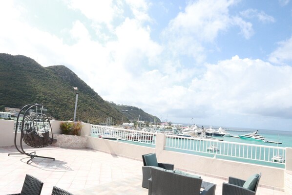 A terrace with wicker furniture, a hanging chair, and a view of boats at a marina.