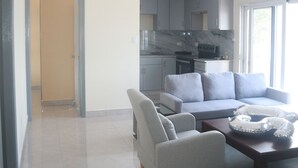 En moderne stue med en grå sofa, et sofabord og et køkken i baggrunden.