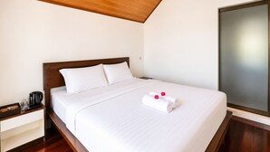 Camera d'albergo con soffitto in legno, un letto grande con lenzuola bianche, un comodino con una macchina da caffè e un'ampia finestra.