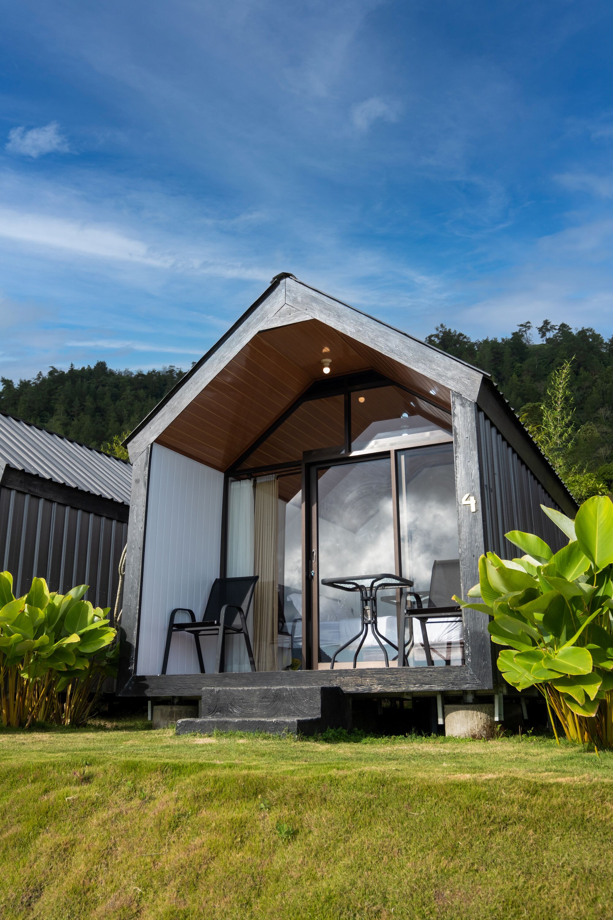 Eine moderne Holzhütte mit überdachter Veranda, großen Fenstern und Blick auf die umliegende Landschaft.