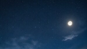 Una fila di cabine con finestre e porte aperte, sullo sfondo di un cielo notturno stellato con una luna visibile.