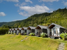A row of cabins with a grassy slope leading up to them, set against a backdrop of a forested hill.