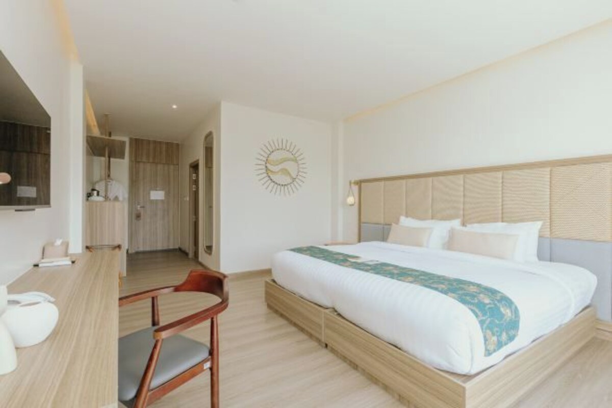 A hotel room with a bed, a desk, a chair, and a wall-mounted clock.