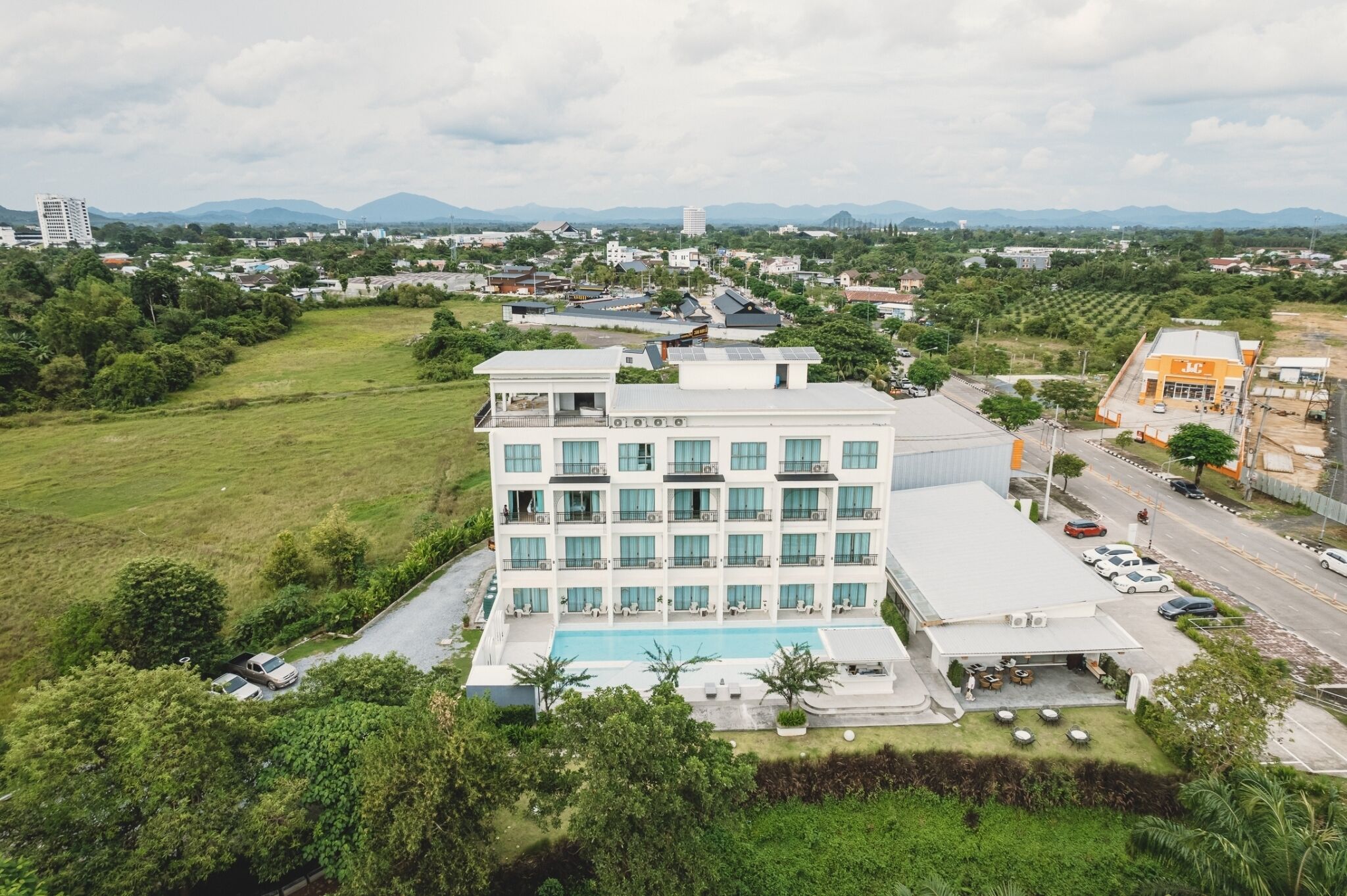A modern hotel with a swimming pool, surrounded by greenery and a view of distant mountains.
