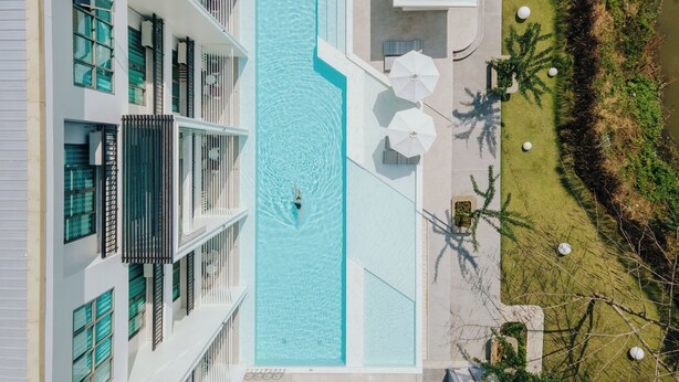 A swimming pool surrounded by a building with balconies and outdoor umbrellas. - Parima Hotel (Trang)