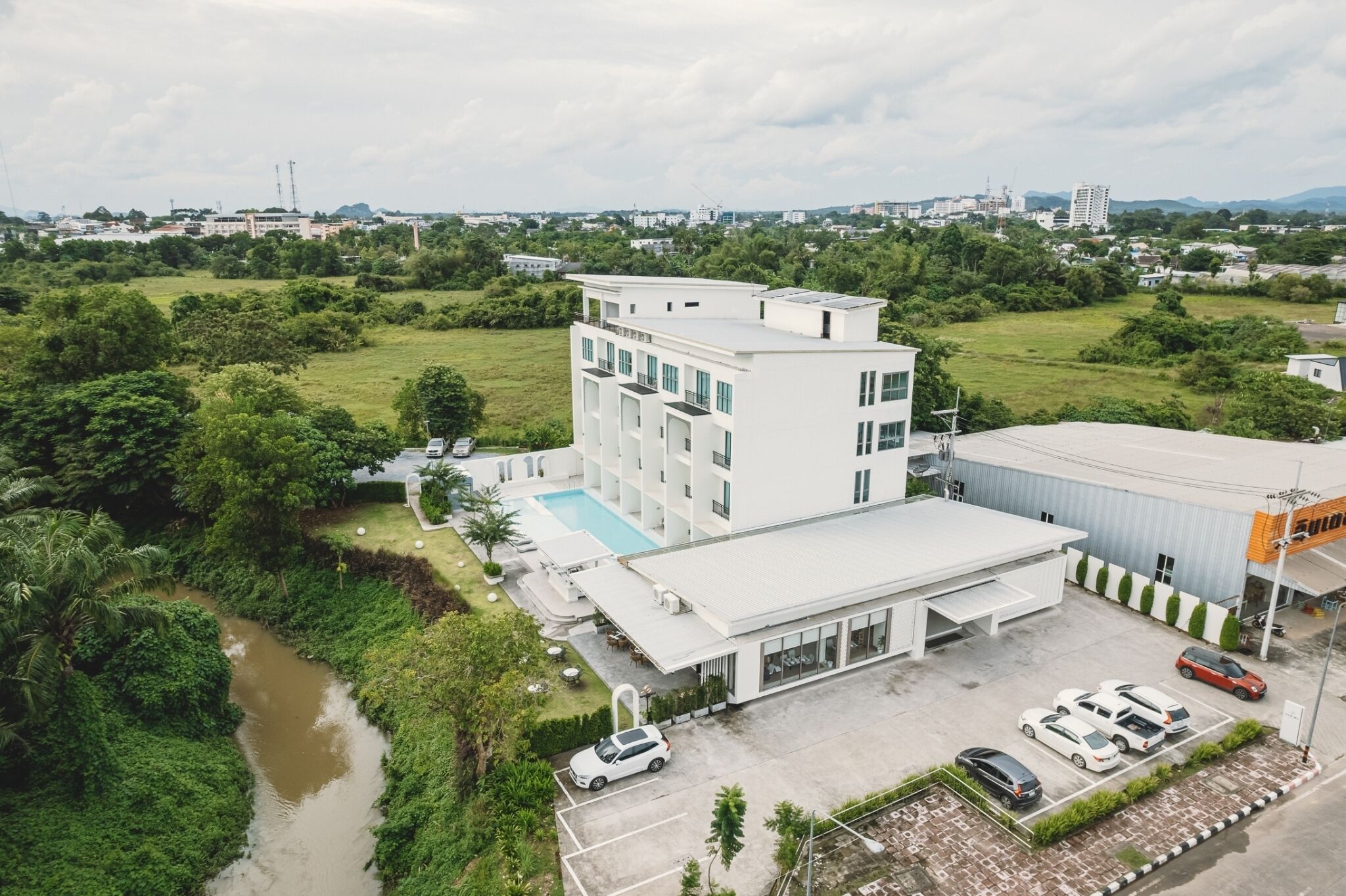 A modern hotel with a swimming pool, surrounded by lush greenery and a river.