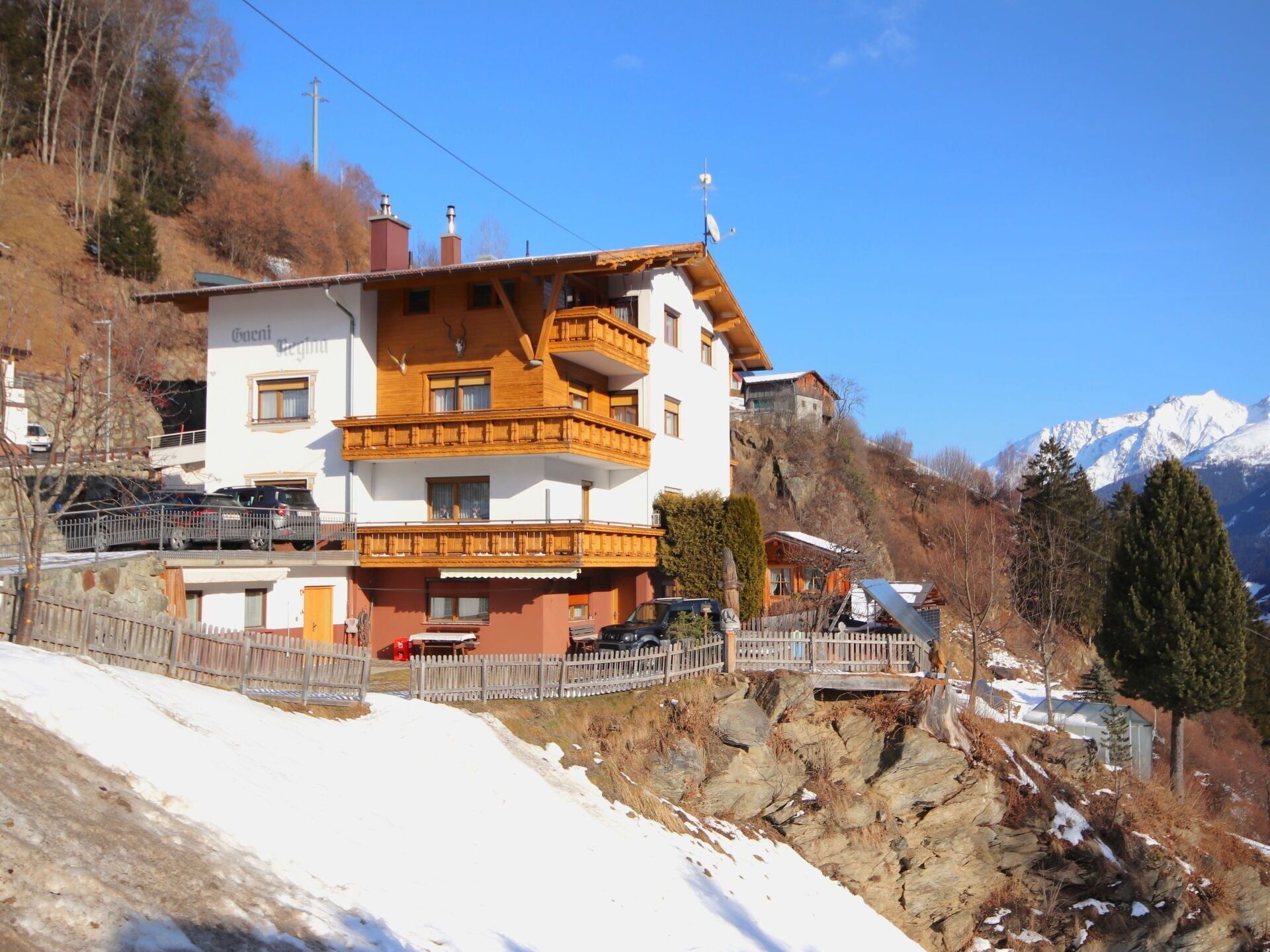 Un edificio a più piani con balconi, posizionato su una collina con vista su montagne innevate.