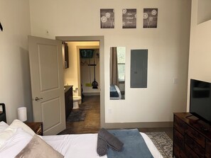 Ett sovrum med en säng, en byrå, en tv och ett badrum som syns genom en öppen dörr.