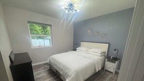 Un dormitorio con cama, mesita de noche, escritorio, ventana y lámpara de techo.