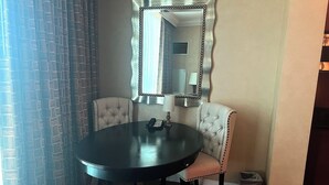 Ein Zimmer mit einem runden Tisch, zwei Polsterstühlen, einem Spiegel mit dekorativem Rahmen und einer Lampe.