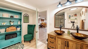 A bathroom with a wooden vanity, a large mirror, and a teal shelving unit with towels and baskets.