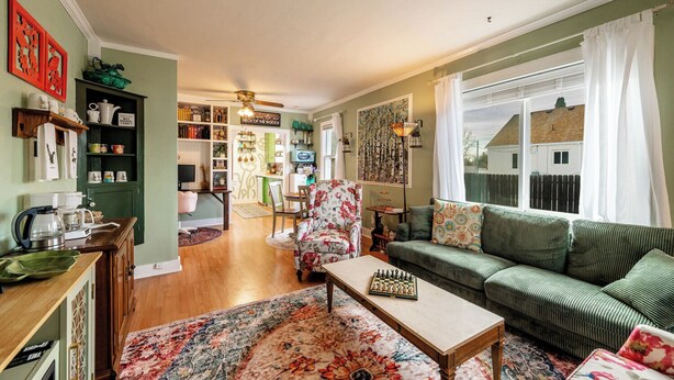 A cozy living room with a sofa, a coffee table, and a chessboard. There is a bookshelf, a dining area, and a kitchen visible in the background.