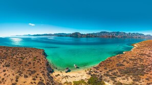 Eine Küstenlandschaft mit klarem türkisblauem Wasser, felsigem Gelände und fernen Bergen.