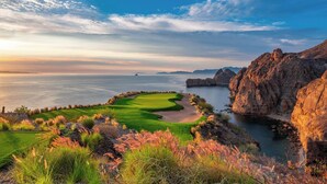 A golf course with a water body and rocky cliffs.