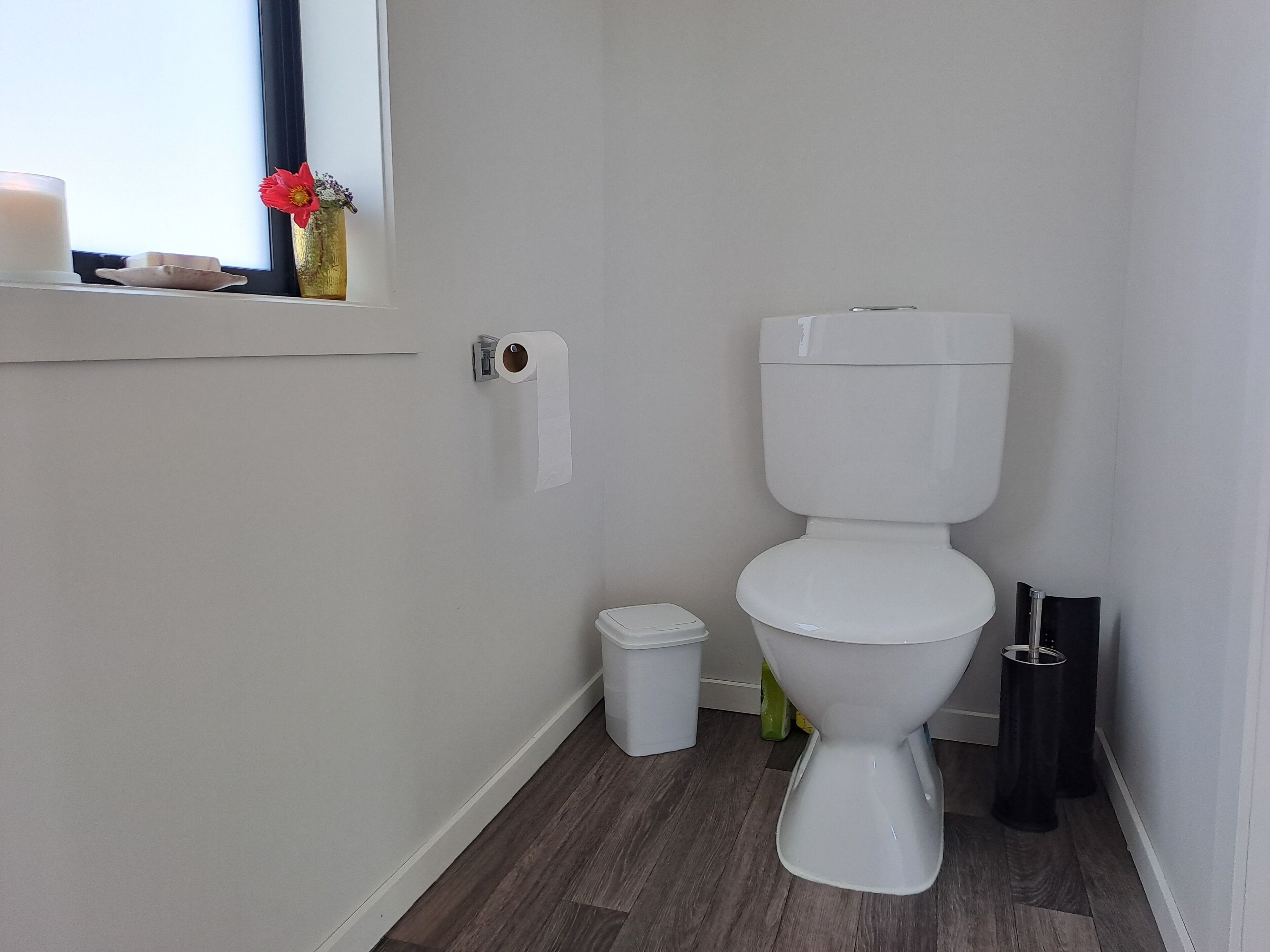 Un baño moderno con inodoro, un cubo de basura pequeño y un dispensador de papel higiénico en la pared.