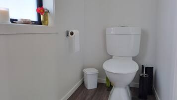 Un baño moderno con inodoro, un cubo de basura pequeño y un dispensador de papel higiénico en la pared.