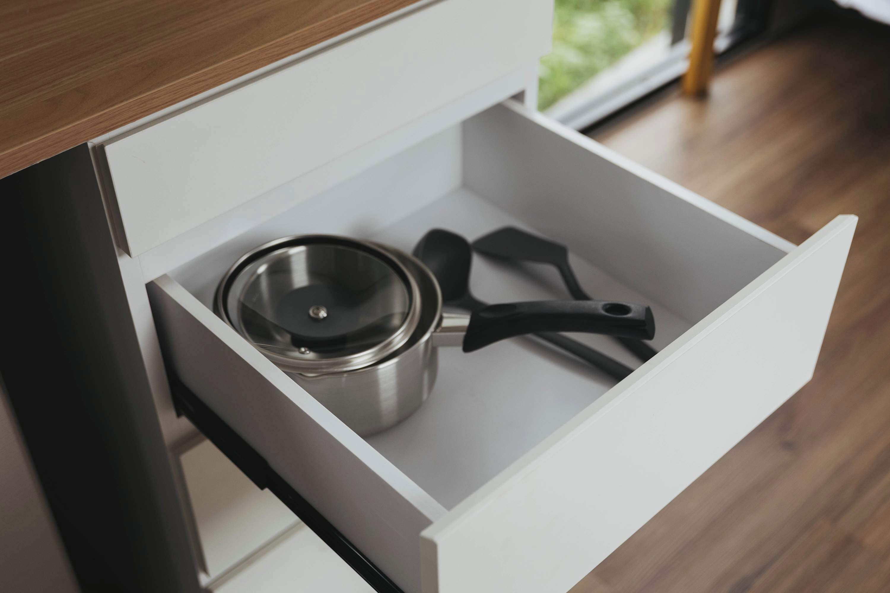 A kitchen drawer containing a stainless steel pot and a black spatula.