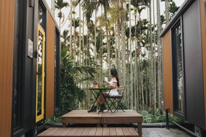 Una mujer sentada a una mesa de madera en un edificio moderno con ventanas amplias y vista a árboles altos.