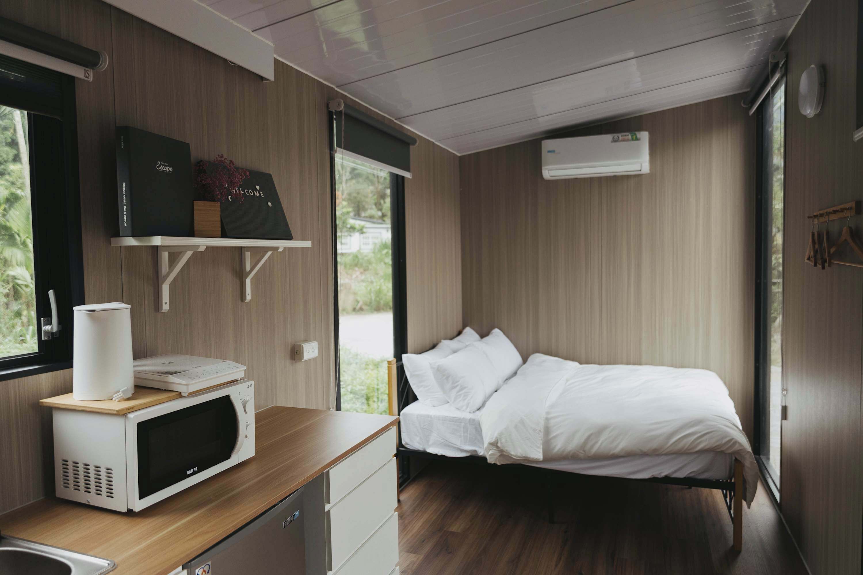 Une petite chambre comprenant un lit, un four à micro-ondes, une petite table en bois et un téléviseur fixé au mur.