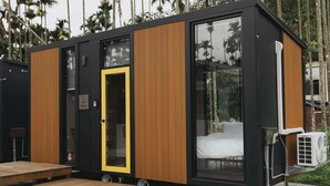 Una cabaña moderna y compacta con puerta corrediza de vidrio, un pequeño espacio de estar al aire libre y un equipo de aire acondicionado.