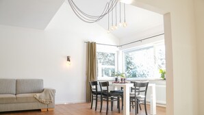 A room with a sofa, dining table, chairs, a hanging light fixture, and a window with a view. - Holiday Home 'Happiness' with Private Terrace, Private Garden and Wi-Fi (Geislingen)