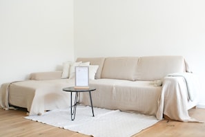 Ein sofasofa in neutraler Farbe mit einem kleinen runden Tisch davor, einem weißen Teppich auf dem Boden und einem Willkommensschild auf dem Tisch.