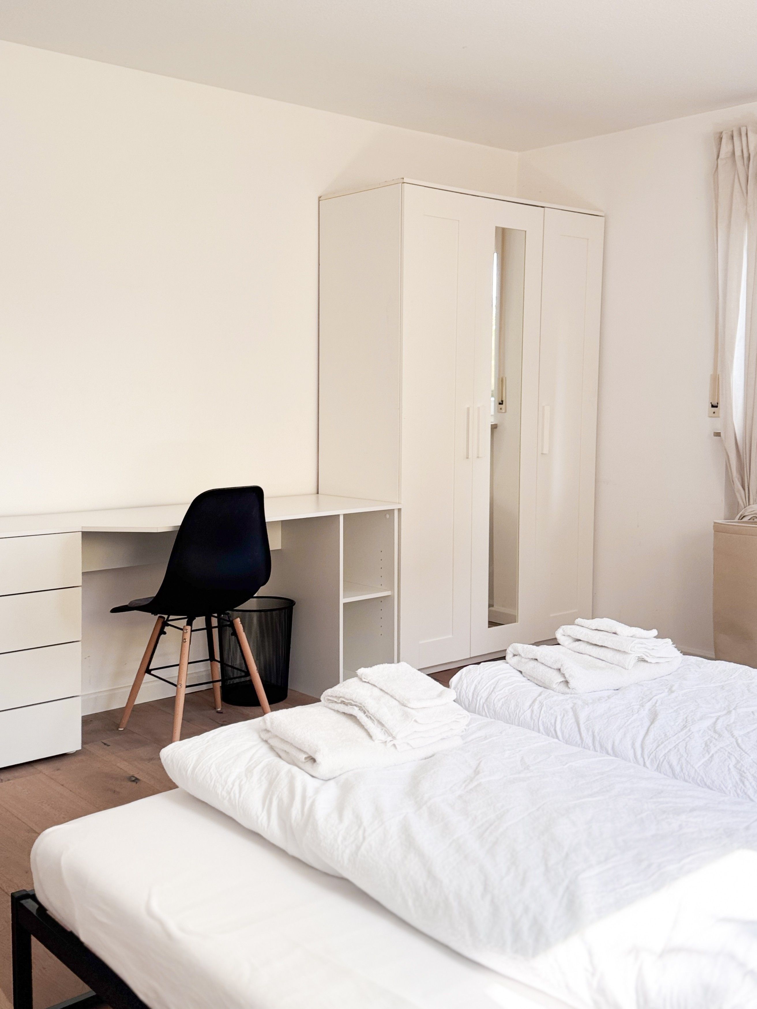 Une chambre à coucher comprenant un lit, un bureau avec une chaise, une armoire et une fenêtre avec des rideaux.