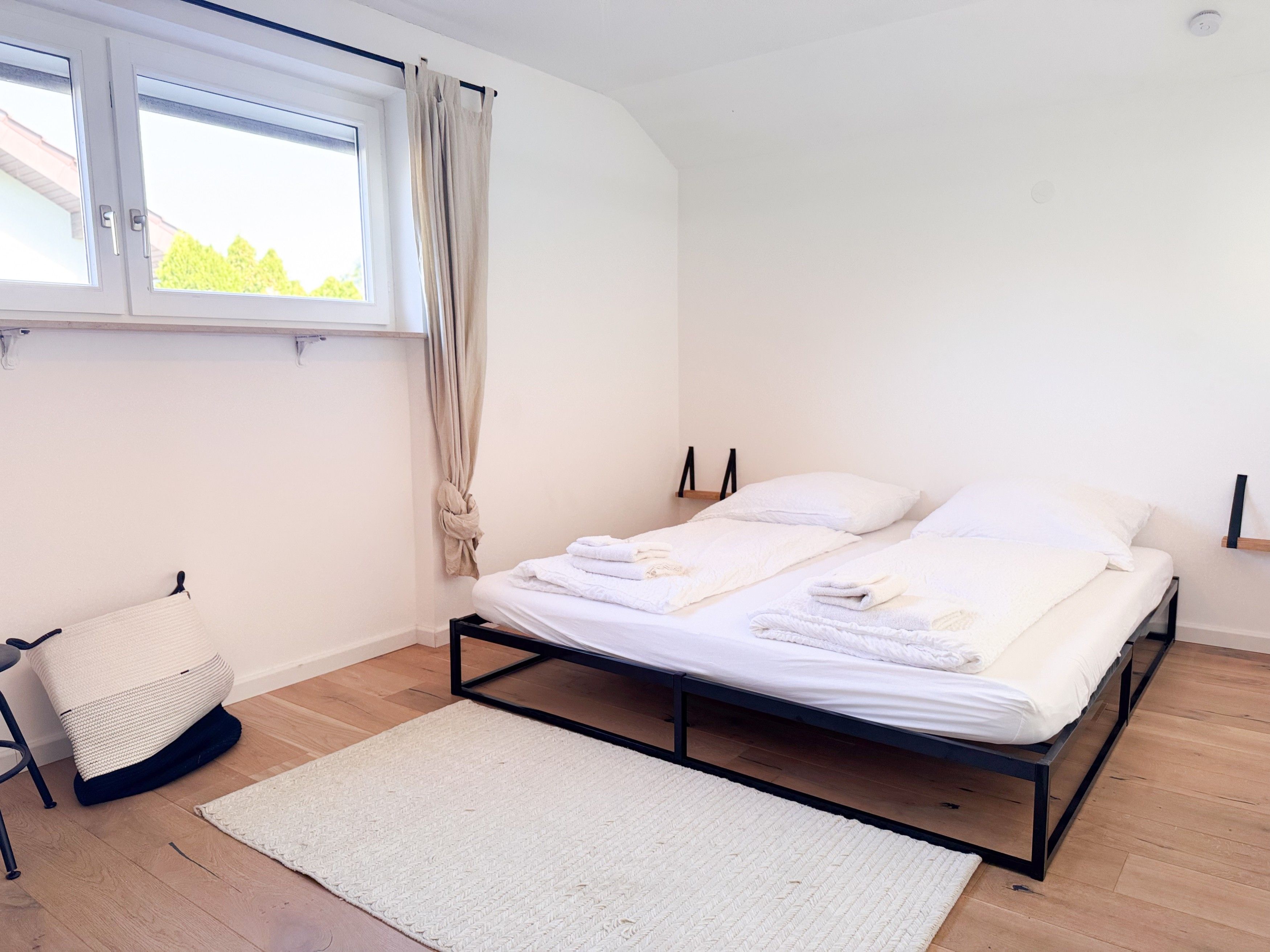 Ein Schlafzimmer mit Bett, Fenster, Vorhang, Nachttisch und Stuhl.