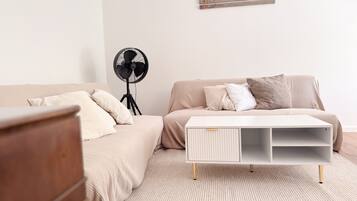A bedroom with a bed, a white side table, a floor fan, and a wall-mounted artwork.