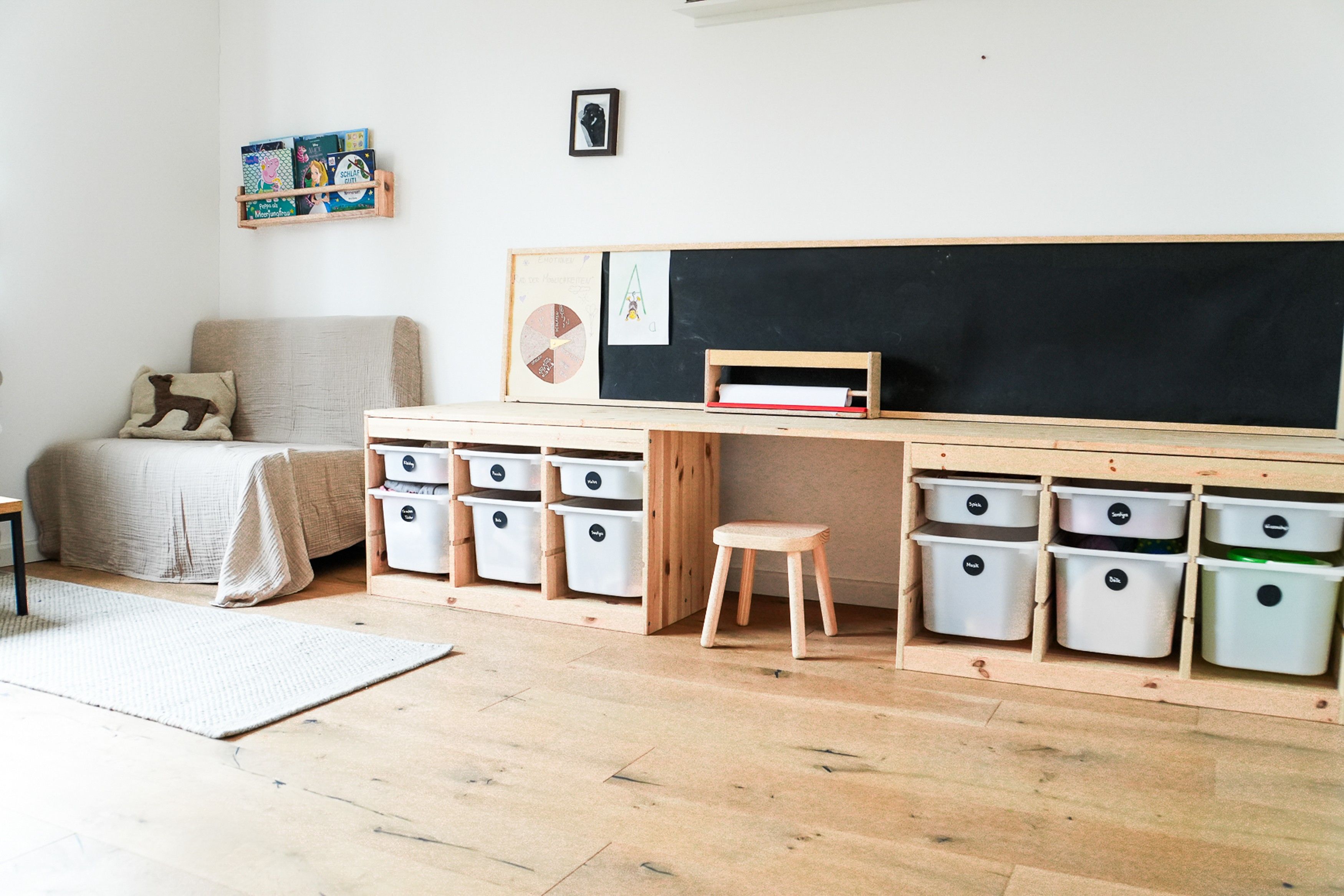 A child's room with a wooden desk, storage bins, a bed, and a chalkboard.