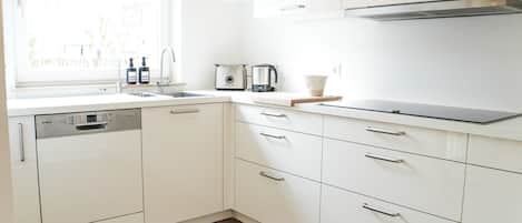 Une cuisine moderne avec des meubles blancs, un lave-vaisselle, un grille-pain et une bouilloire.