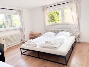 A bedroom with a bed, a radiator, a window with curtains, and a wooden nightstand. - Holiday Home 'Landhausglück' with Private Terrace, Private Garden and Wi-Fi (Geislingen)