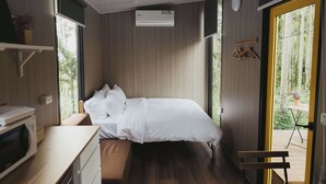 Une chambre moderne avec un lit, un bureau et une petite table. Une fenêtre offre une vue sur la verdure environnante.