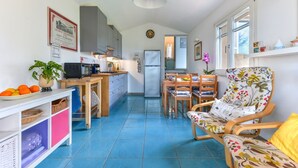 A compact kitchen with a refrigerator, microwave, and sink. There is a dining area with a table and chairs, and a chair with a floral pattern. - Casa Vignola, Capoliveri (Capoliveri)