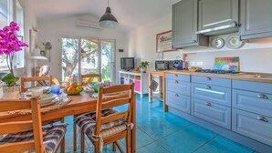A kitchen with grey cabinets, a dining table with chairs, a TV, and a microwave. - Casa Vignola, Capoliveri (Capoliveri)