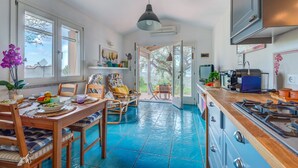 A kitchen with a blue tiled floor, wooden furniture, a dining table with chairs, a hanging light fixture, and a view through a glass door. - Casa Vignola, Capoliveri (Capoliveri)