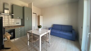 Eine moderne Küche mit Esstisch und Stühlen, ein blaues Sofa und ein kleiner Fernseher.