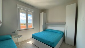 Ein Schlafzimmer mit einem Bett, einem kleinen Tisch, einem Kleiderschrank und einem Fenster mit Blick auf Gebäude.