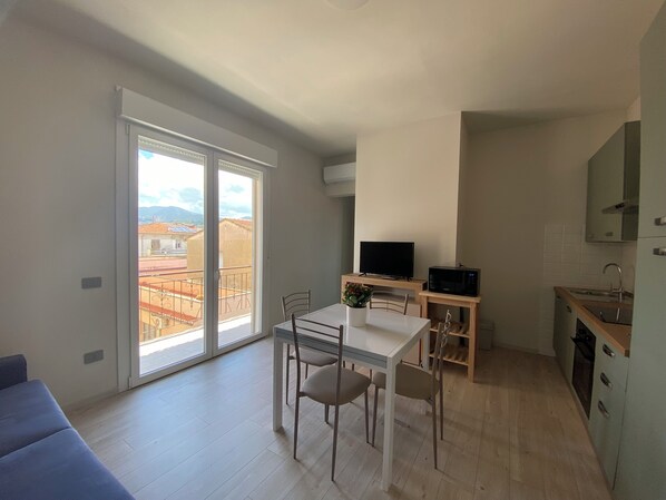 A modern apartment with a balcony, a dining area, a kitchen, and a TV.