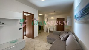 Un salon moderne avec un canapé, un coin repas comprenant une table et des chaises, et une cuisine en arrière-plan.